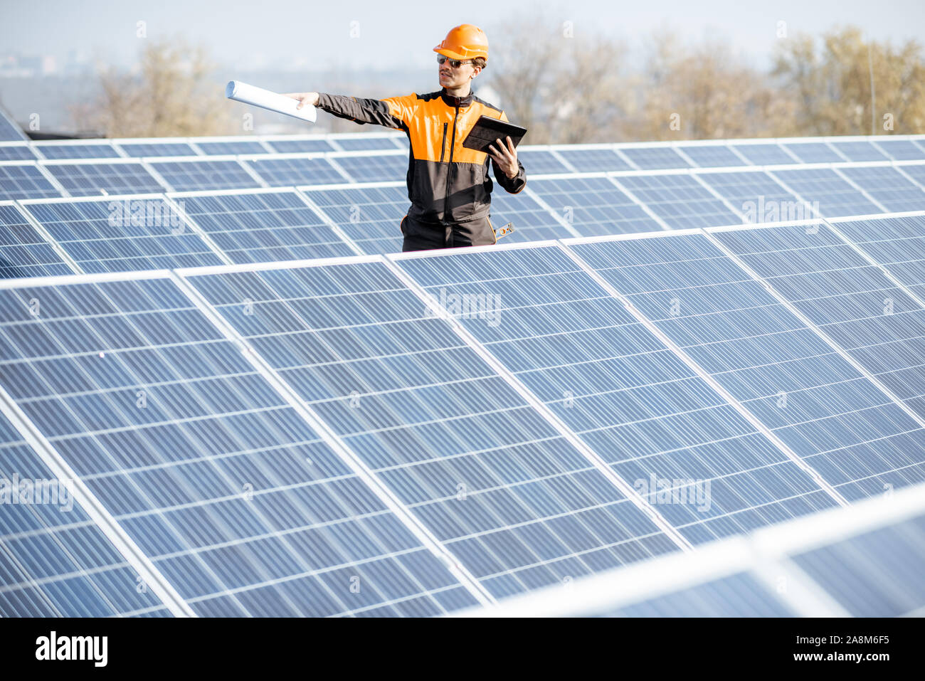 Ansicht auf dem Dach Solarkraftwerk mit Ingenieur in arbeitsschutzausrüstungen Wandern und Prüfung von Photovoltaik-Modulen. Konzept der alternativen Energie und deren Wartung Stockfoto