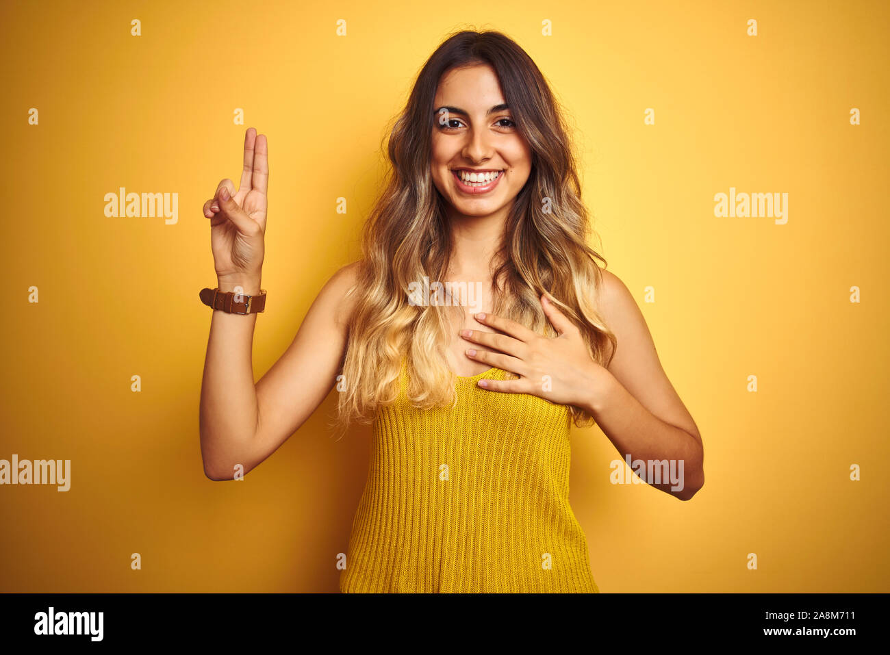 Junge schöne Frau in t-shirt in gelb isoliert Hintergrund lächelnd Vereidigung mit der Hand auf der Brust und die Finger nach oben, und eine Loyalität versprechen Oat Stockfoto