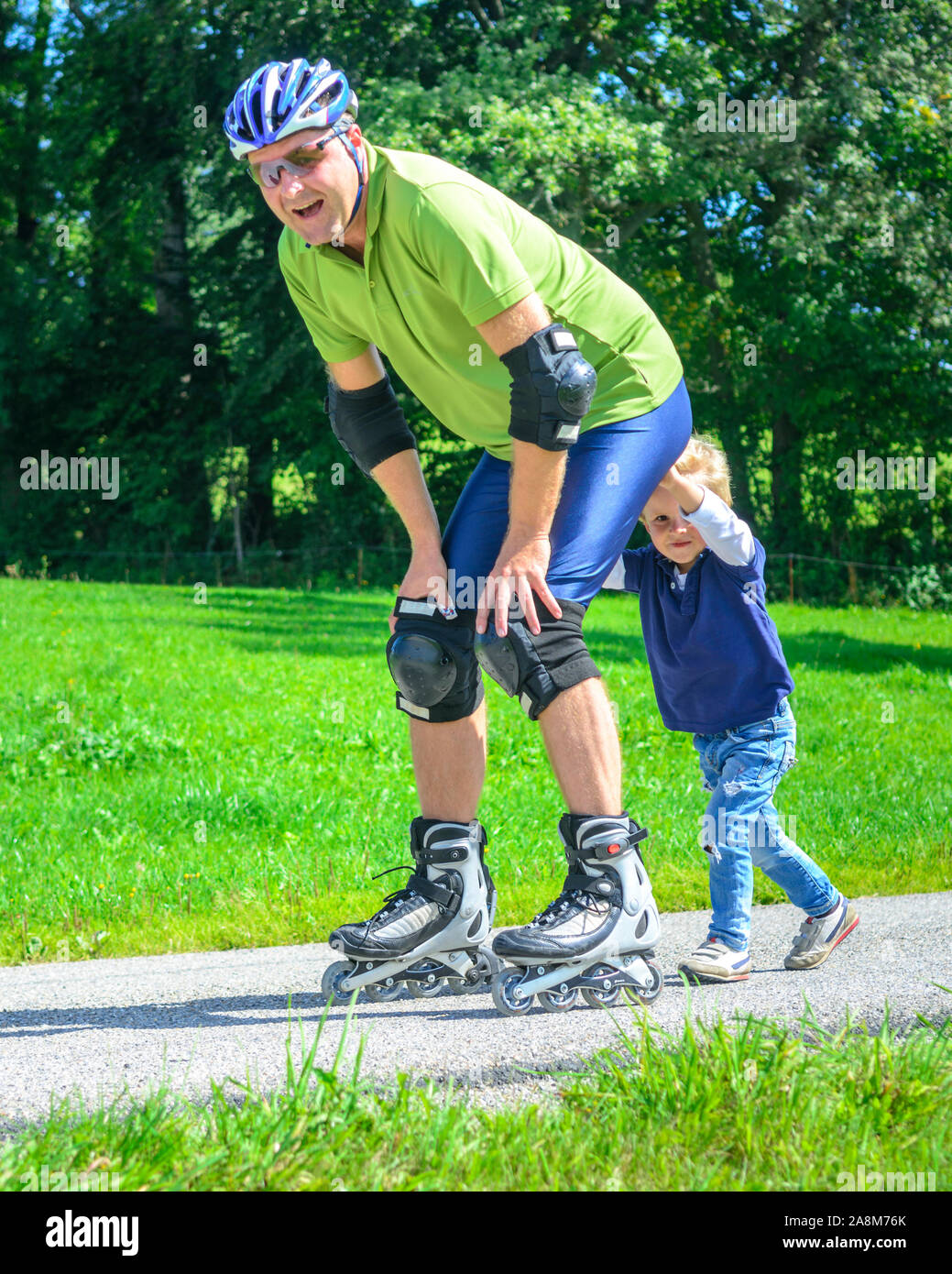 Mann eine skating Tour auf Inline Skates mit Hilfe seines kleinen Sohnes in der grünen Natur Stockfoto