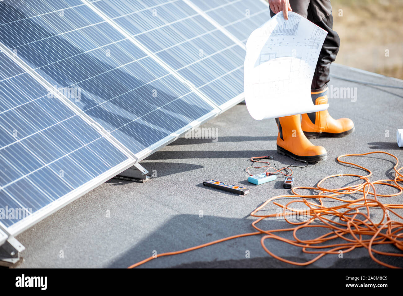 Die Installation von Sonnenkollektoren, close-up auf eine funktionierende Tools. Drähte und Mann in Schutzkleidung stehen auf einer Dachterrasse mit PV-Kraftwerk Stockfoto