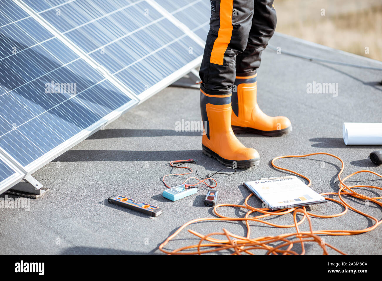 Die Installation von Sonnenkollektoren, close-up auf eine funktionierende Tools. Drähte und Mann in Schutzkleidung stehen auf einer Dachterrasse mit PV-Kraftwerk Stockfoto