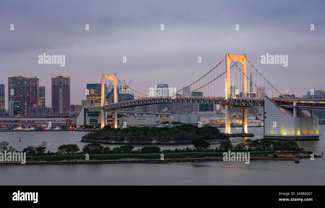 Blick auf die Skyline mit Wolkenkratzern und beleuchtete Rainbow Bridge am Abend, Odaiba, Tokio, Japan Stockfoto