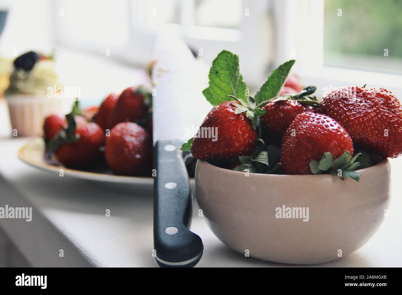 Frische schmackhaft und lecker Erdbeeren in einer weißen Schüssel auf ein Fenster im Hintergrund. Gesunde Ernährung und Lebensmittel Konzept, Vitamine für den Herbst Gesundheit. Hell Stockfoto