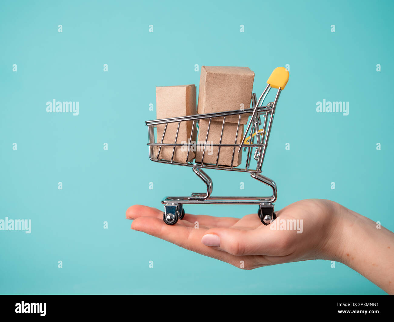 Spielzeug Warenkorb mit Boxen in weiblicher Hand über blauen Hintergrund. Kopieren Sie Platz für Text oder Design. Ssale, Rabatt, shopaholism Konzept. Konsumgesellschaft Trend Stockfoto