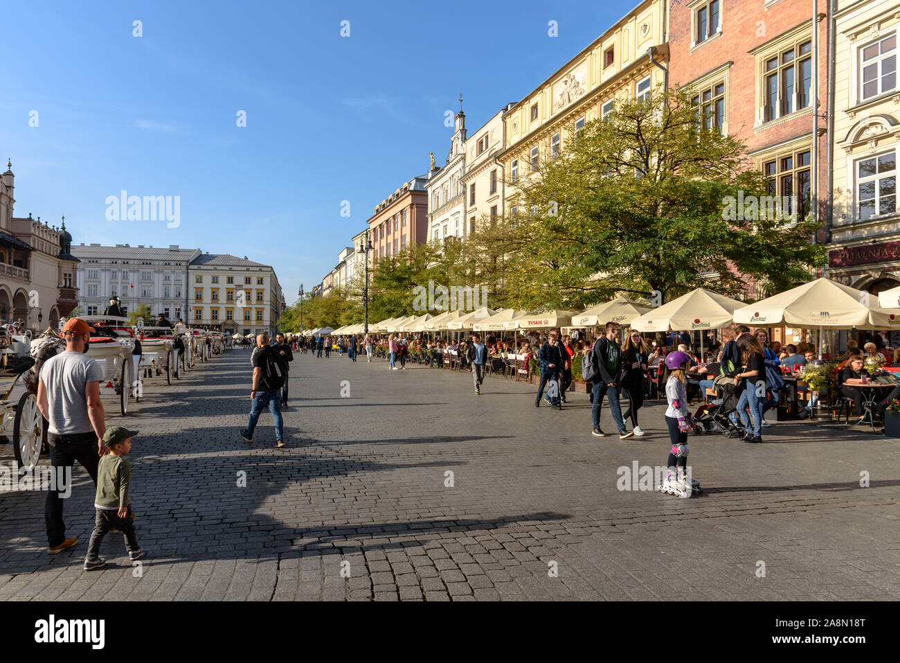 Menschen sitzen unter Sonnenschirmen auf Terrassen am Hauptplatz der Altstadt in Krakau, Polen an einem sonnigen Herbsttag Stockfoto