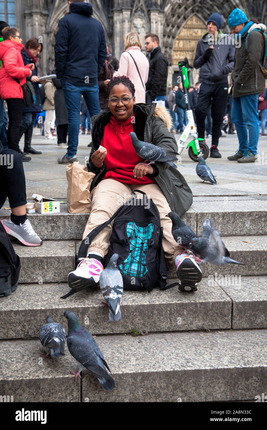 Junge Frau füttern verwilderter Tauben vor der Kathedrale, Köln, Deutschland junge Frau fuettert Stadttauben vor dem Dom, Köln, Deutschland. Stockfoto