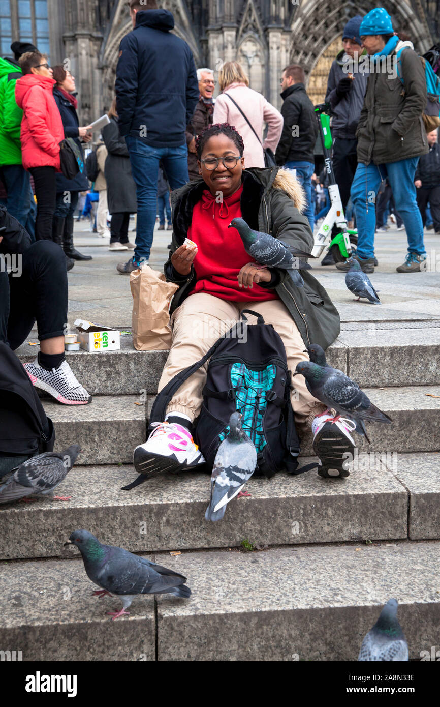 Junge Frau füttern verwilderter Tauben vor der Kathedrale, Köln, Deutschland junge Frau fuettert Stadttauben vor dem Dom, Köln, Deutschland. Stockfoto