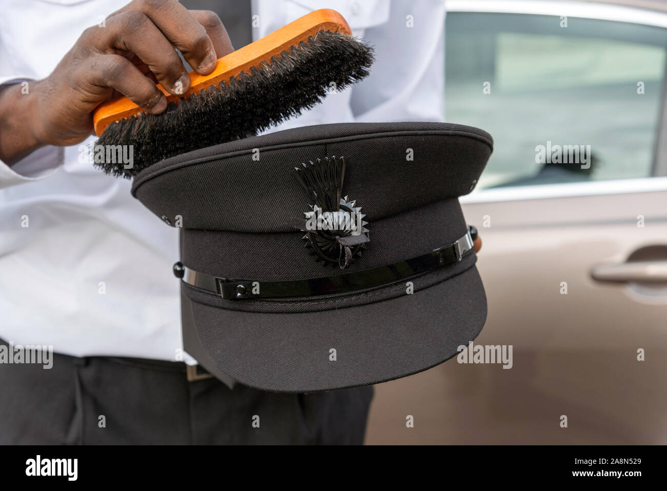 Andover, England, UK. Oktober 2019. Chauffeur Bürsten den Staub von seinen schwarzen Uniform hat. Stockfoto