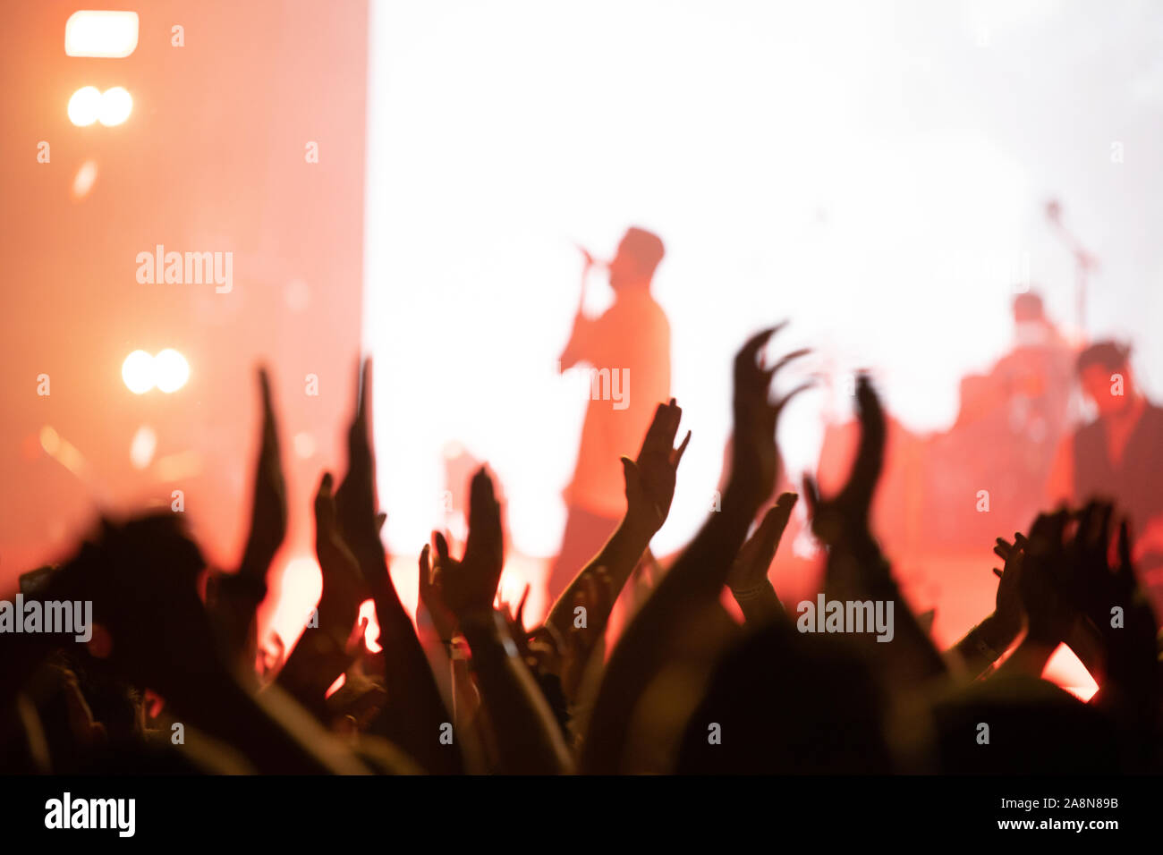 Aus der Masse mit den Händen klatschen bei einem Konzert mit einer hellen Bühne und verschwommenes Sänger. Stockfoto