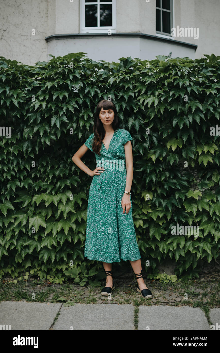 Frau mit einem eleganten grünen Kleid steht vor der Hedge Stockfoto