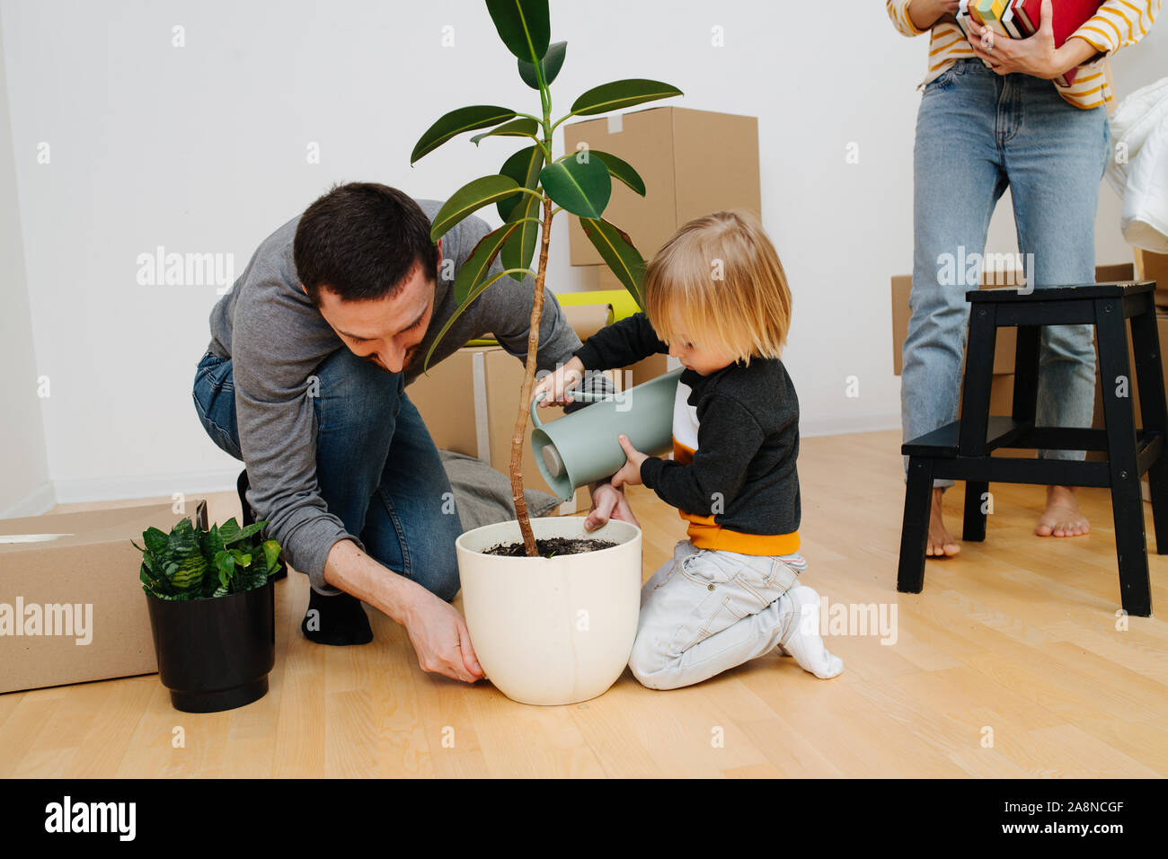 Familie zog in eine neue Wohnung. Kind Bewässerung Anlage während Eltern auspacken. Stockfoto