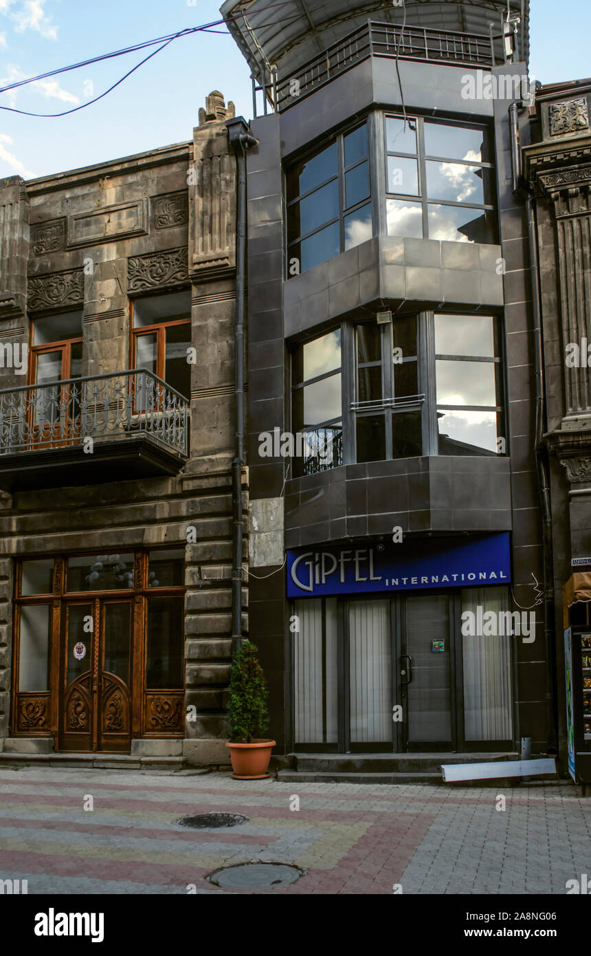 Gyumri, Armenien, 05. September 2019: Ein schmales Gebäude von einem modernen Einkaufszentrum aus dunklem Stein mit großen Fenstern zwischen alten Gebäuden o Stockfoto