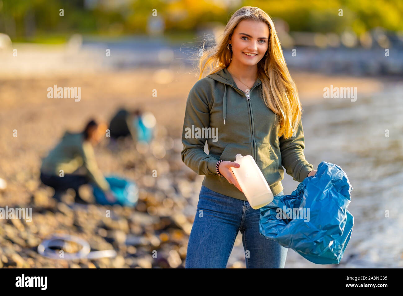 Freiwillige holding Flasche und müllsack am Strand Stockfoto