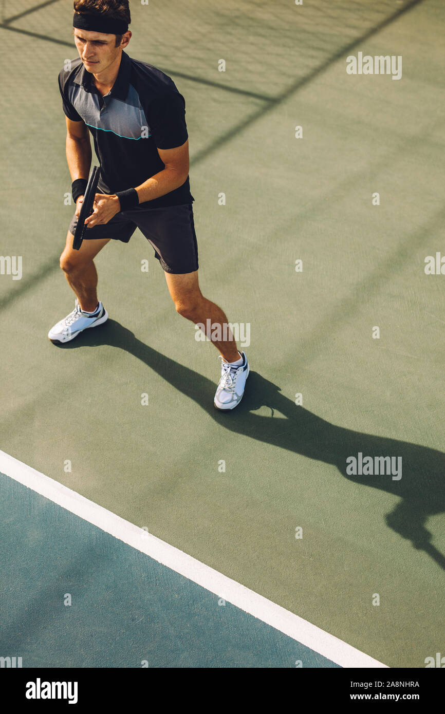 High Angle Shot eines männlichen Tennisspieler Tennis spielen auf hartplatz. Junge Mann in Sportkleidung auf dem Tennisplatz baseline Bereit zurückzukehren, die Stockfoto