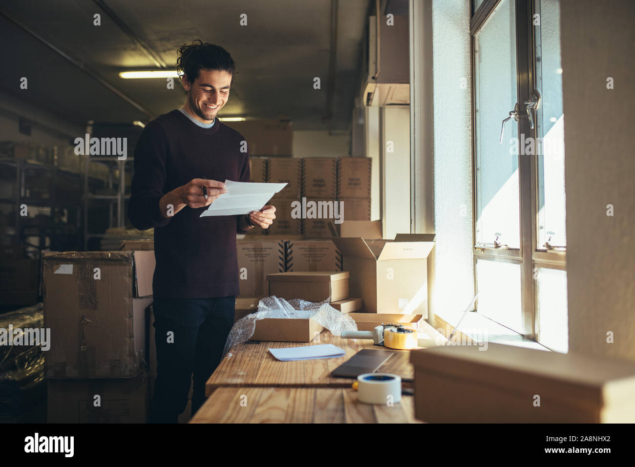 Junger Mann mit einem Papier in der Hand steht die Verpackung im Büro. Online store Inhaber arbeiten im Büro. Stockfoto