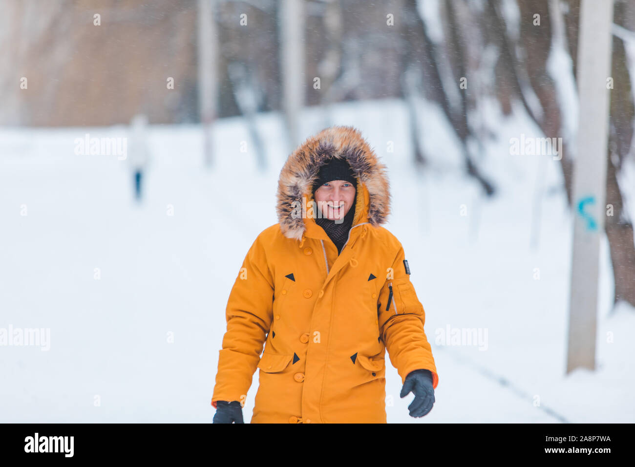 Mann in Gelb winter Mantel mit Kapuze zu Fuß durch die verschneiten Park Stockfoto