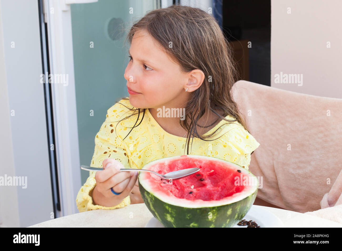Wenig kaukasische Mädchen isst aufgeschnittenen Wassermelone mit einem Löffel, Outdoor Sommer portrait Stockfoto