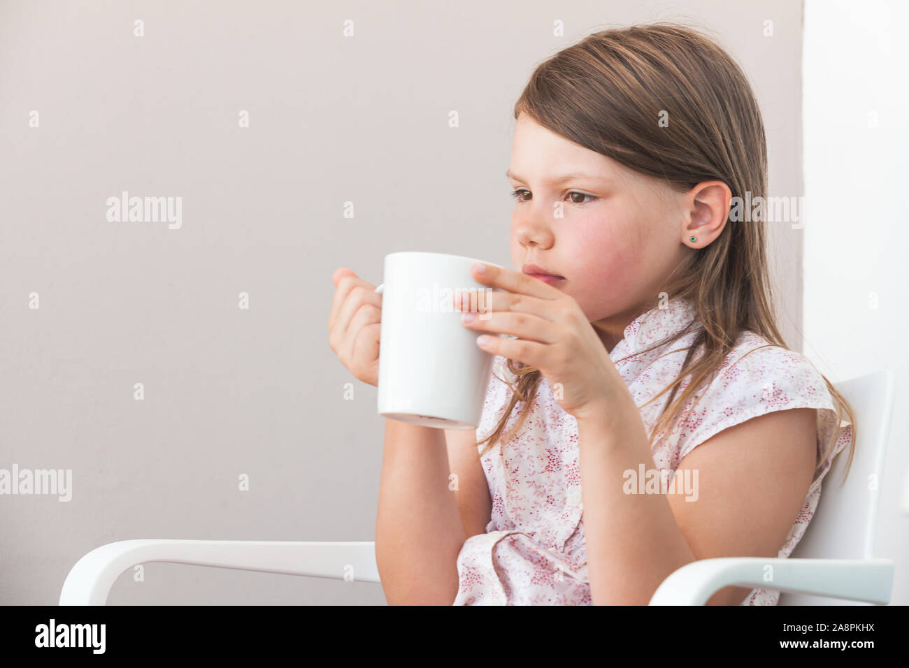 Portrait von kleinen Mädchen mit weißen Tasse heißes Getränk, Nahaufnahme über graues Balkon Wand Hintergrund Stockfoto