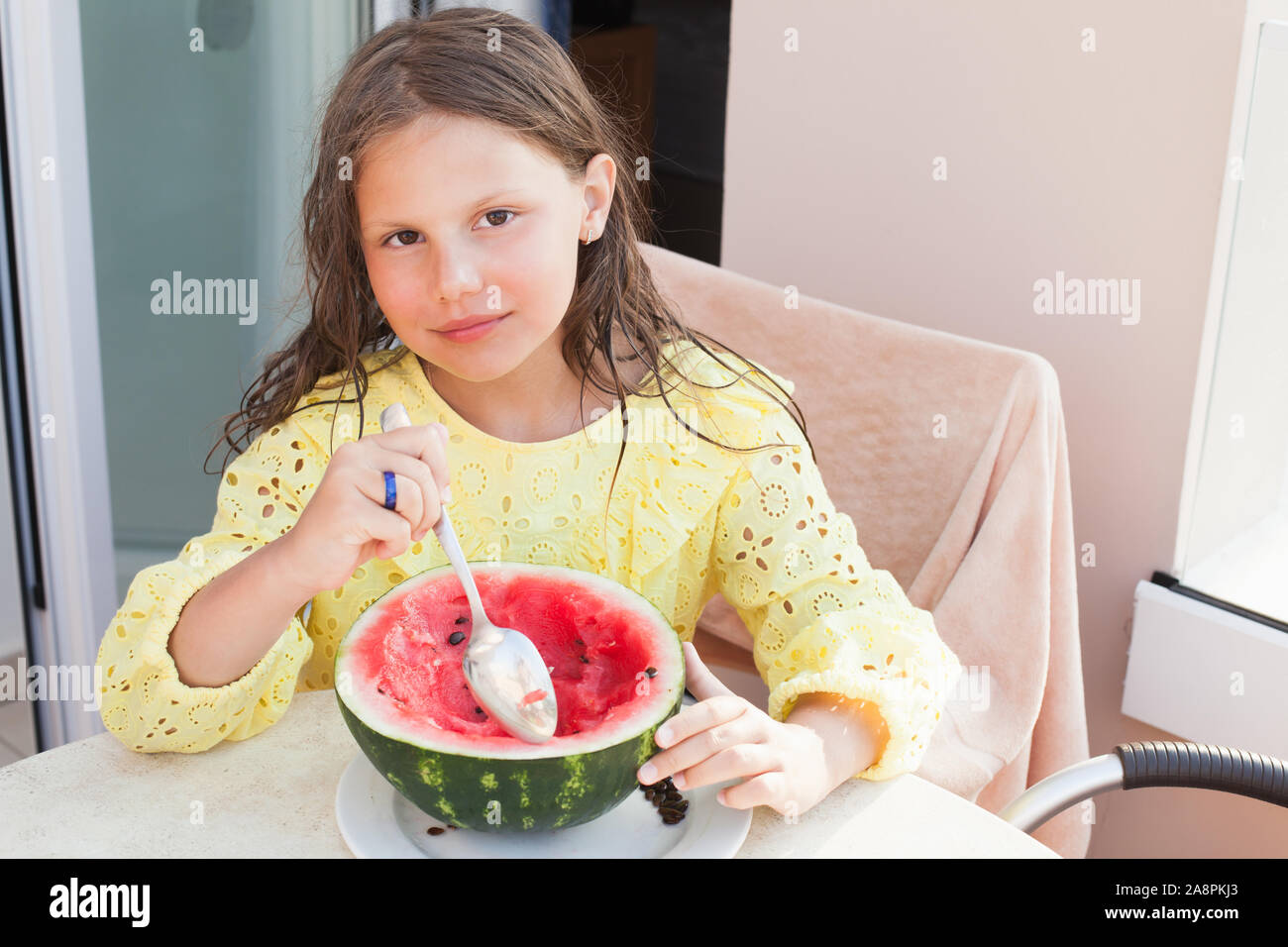 Lächelnde Mädchen isst aufgeschnittenen Wassermelone mit einem Löffel auf einen Balkon, im Sommer portrait Stockfoto