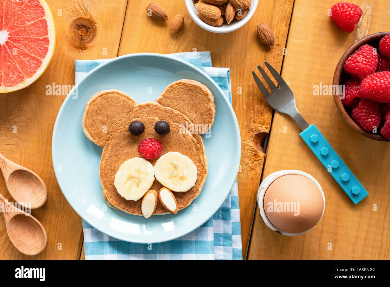 Baby oder Kind Frühstück Pfannkuchen in der Form des Hundes. Lustige Frühstück für Kinder mit Pfannkuchen, Obst und gekochtem Ei auf einem Holztisch. Ansicht von oben Stockfoto