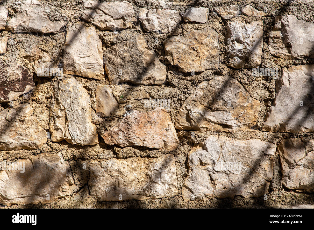 Eine grobe errichtete Steinmauer mit Schatten bilden Gestreifte verlaufende Linien von oben nach unten. Stockfoto