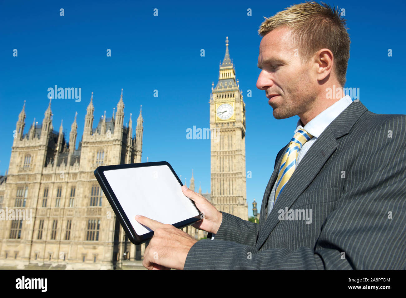 Der britische Politiker verwendet Tablet-Computer vor den Parlamentshäusern und Big Ben unter hellem, sonnigen Himmel in London, Großbritannien Stockfoto