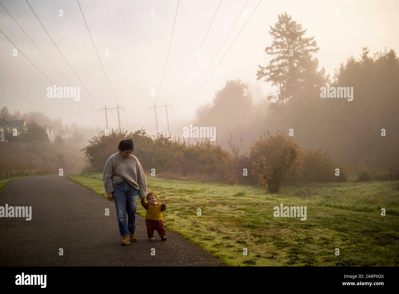Eine Mutter und ihr Baby Spaziergang auf einem gepflasterten Weg im dichten Morgennebel. Stockfoto