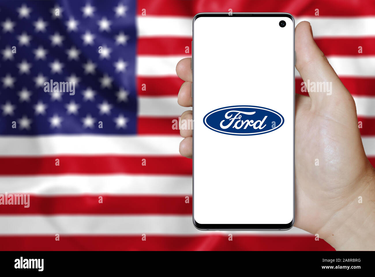 Logo der öffentlichen Unternehmen Ford Motor angezeigt auf einem Smartphone. Flagge der USA Hintergrund. Credit: PIXDUCE Stockfoto