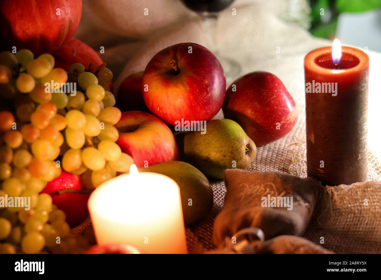 Weiße Trauben Sultana rote Äpfel und Birnen mit Kerzen im Herbst Obst und Gemüse immer noch Leben auf einem Sack Stockfoto