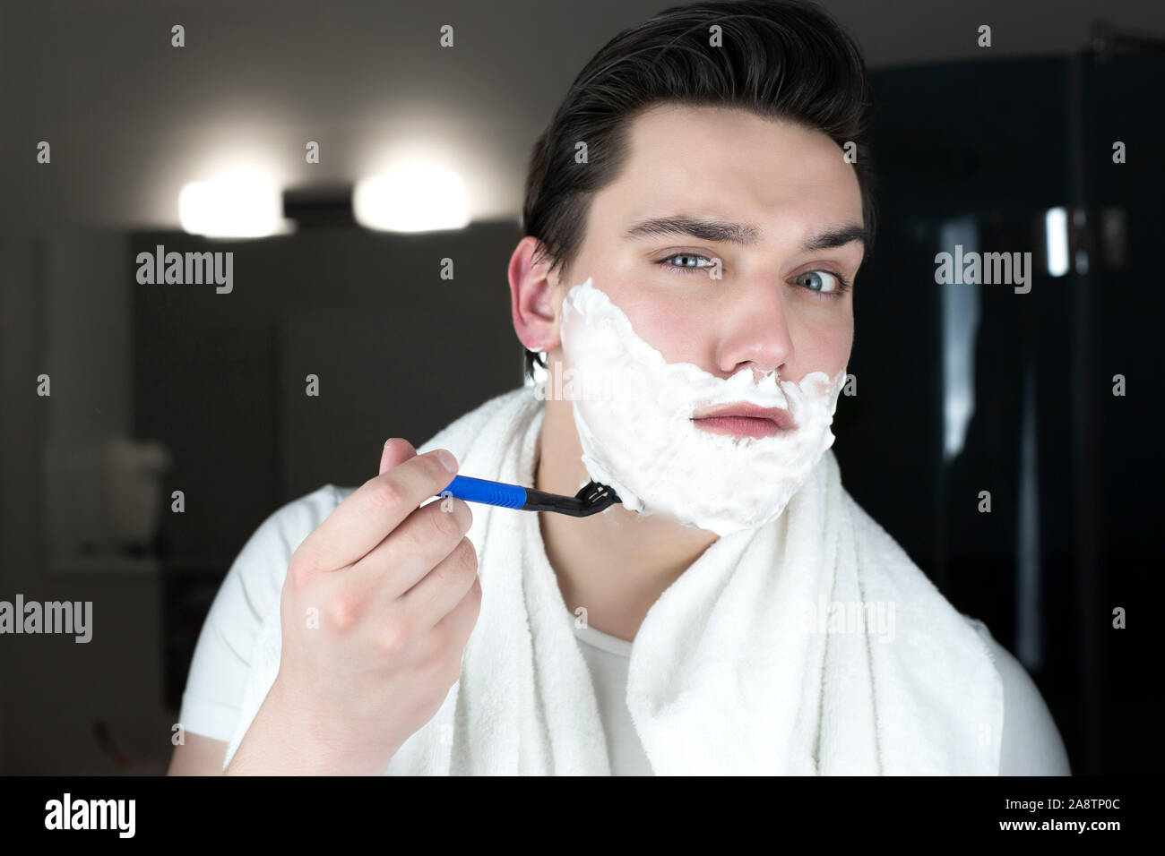 Junger stattlicher Mann mit Schaum auf seinem Gesicht Spaß beim Rasieren im Badezimmer am Morgen Alltag. Stockfoto