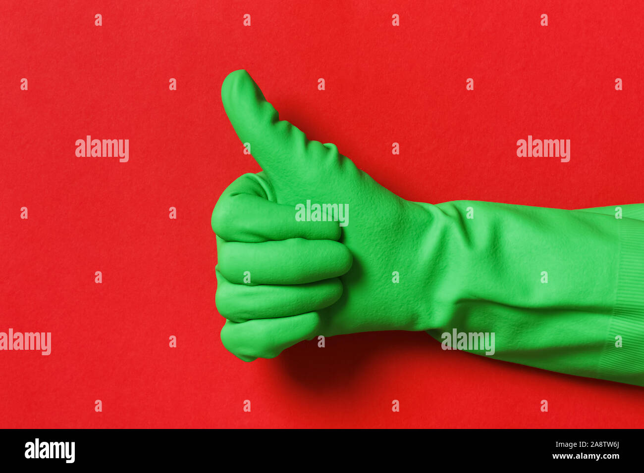 Daumen hoch in einem schutzhandschuh der grünen Farbe auf einem roten Hintergrund. Stockfoto