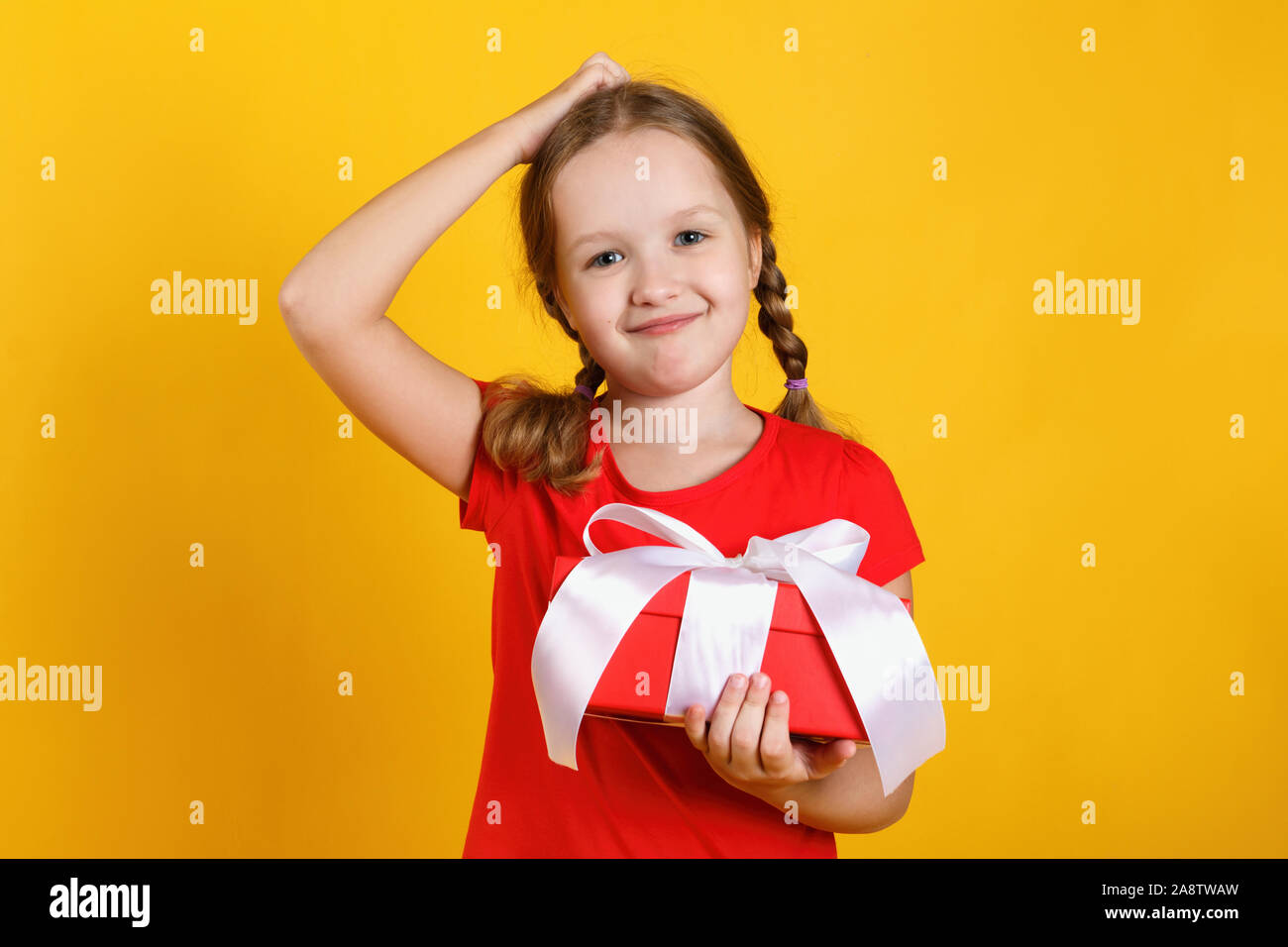 Süßes kleines Mädchen hält einen Kasten mit einem Geschenk. Das Kind fragt, was drin ist. Stockfoto