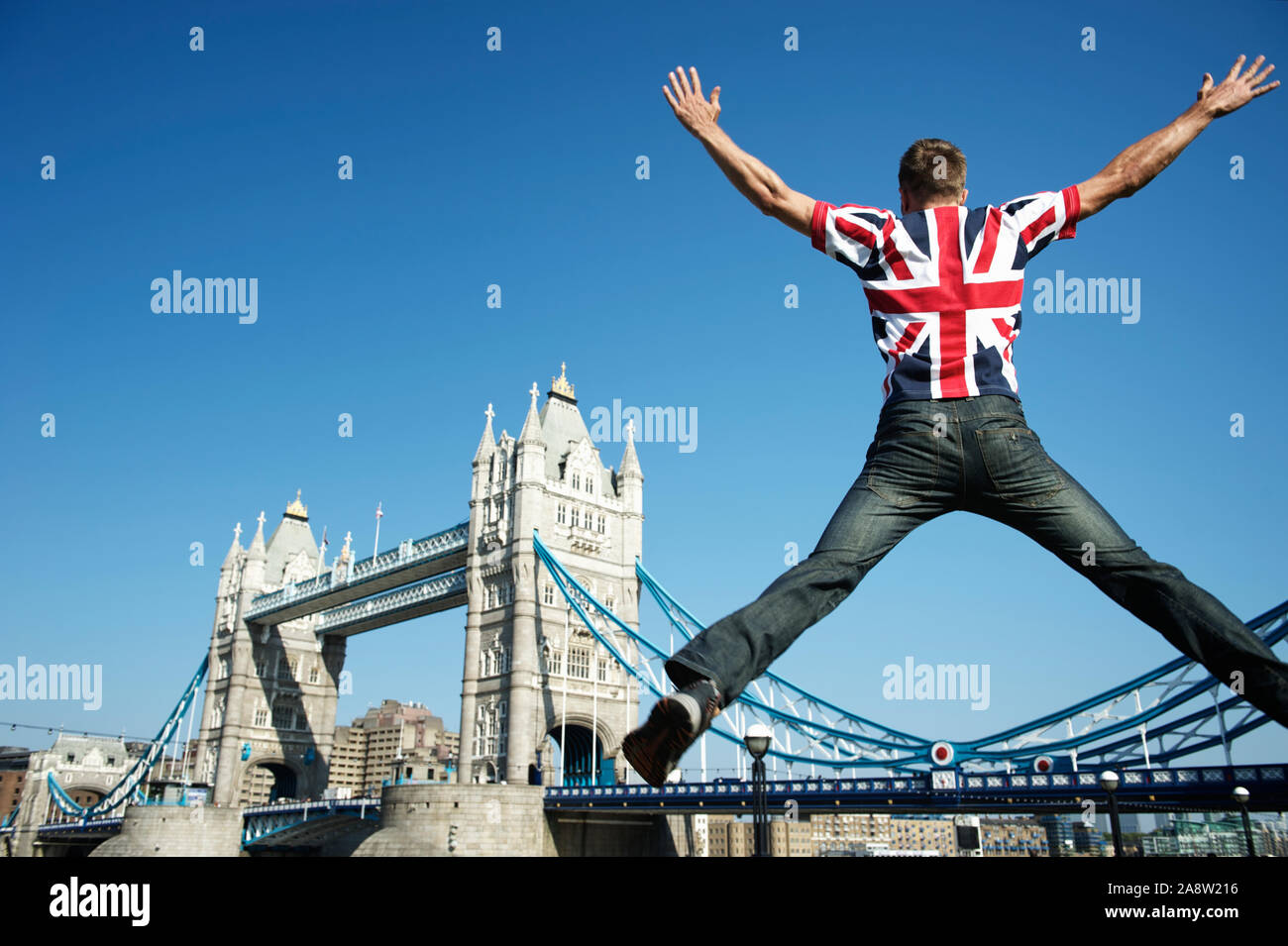 Patriotischer junger britischer Mann, der in einem Union Jack-T-Shirt vor der Tower Bridge, London, springt Stockfoto