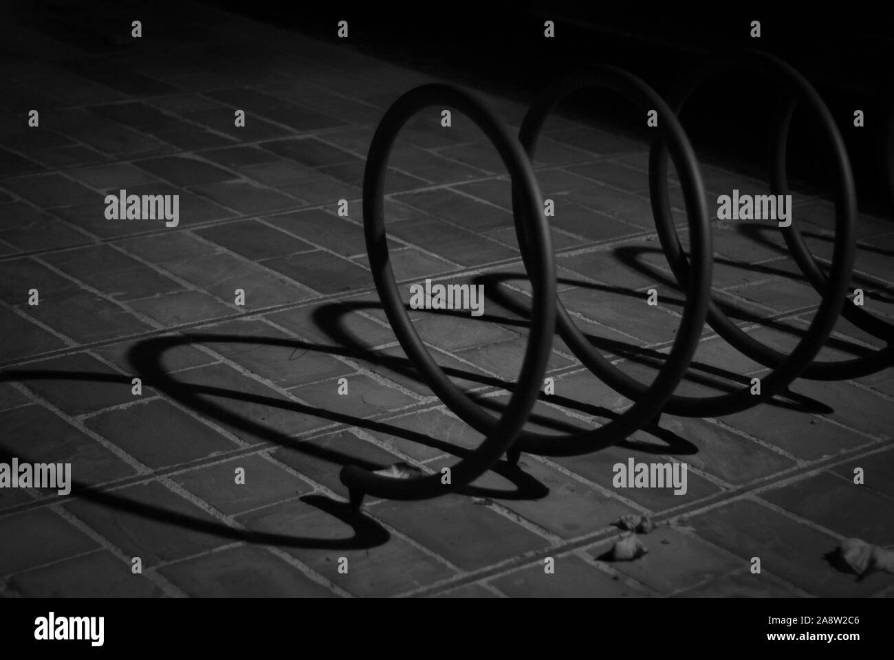 Monochromatische Schuß von Schatten und Lichtern erstellt von eine Straßenlaterne, der nachts eine Spirale für Fahrrad Unterstützung leuchtet Stockfoto