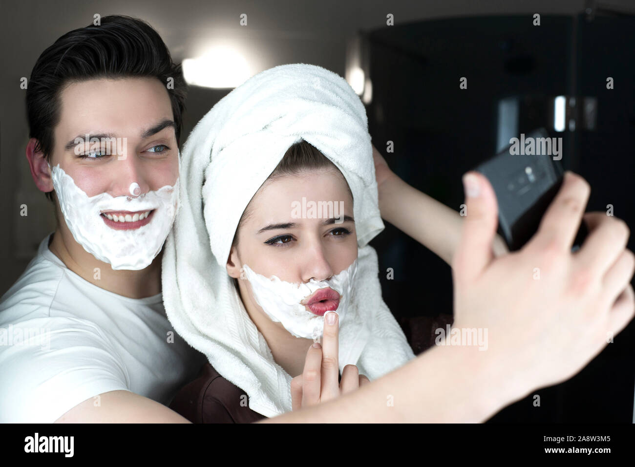Lustig Paar gutaussehenden Mann und schöne Frau ein für selfie suchen lustige sowohl mit Rasierschaum auf ihren Gesichtern in Bad spielerische darstellen. Stockfoto