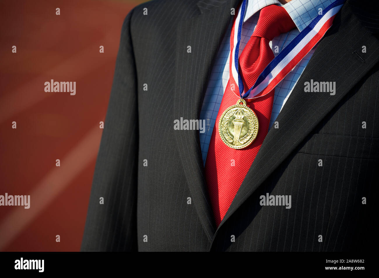 Goldmedaille hängen auf der roten Krawatte von Eine nicht erkennbare Geschäftsmann stand im Freien mit einem Sport Track im Hintergrund Stockfoto