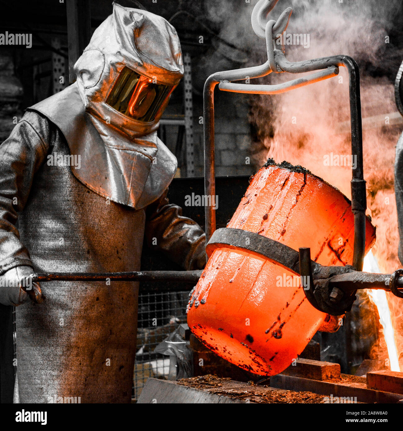 In einer Gießerei-Werkstatt. Ein Arbeitnehmer, der von einem Anzug geschützt gießt die Schmelze in eine Form Stockfoto