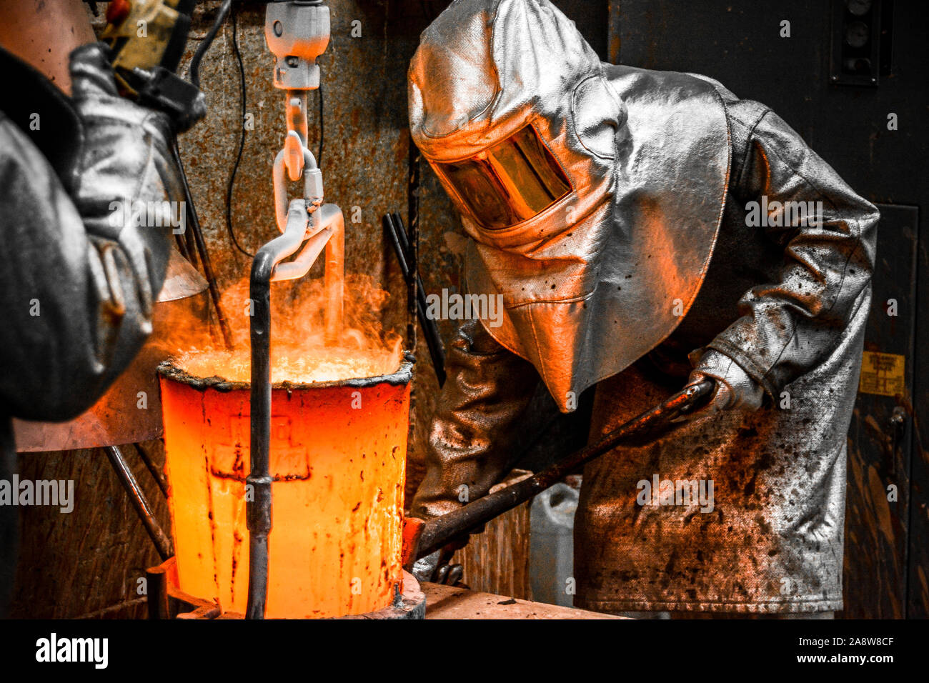 In einer Gießerei-Werkstatt. Arbeiter durch ihre Sicherheitseinrichtungen geschützt Griff ein Tiegel mit geschmolzenem Metall Stockfoto