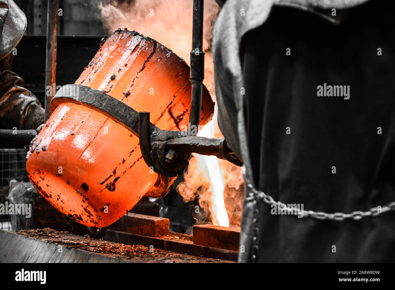In einer Gießerei-Werkstatt. Das geschmolzene Metall wird in eine Form aus einem Tiegel ausgegossen durch zwei Arbeiter manövriert Stockfoto