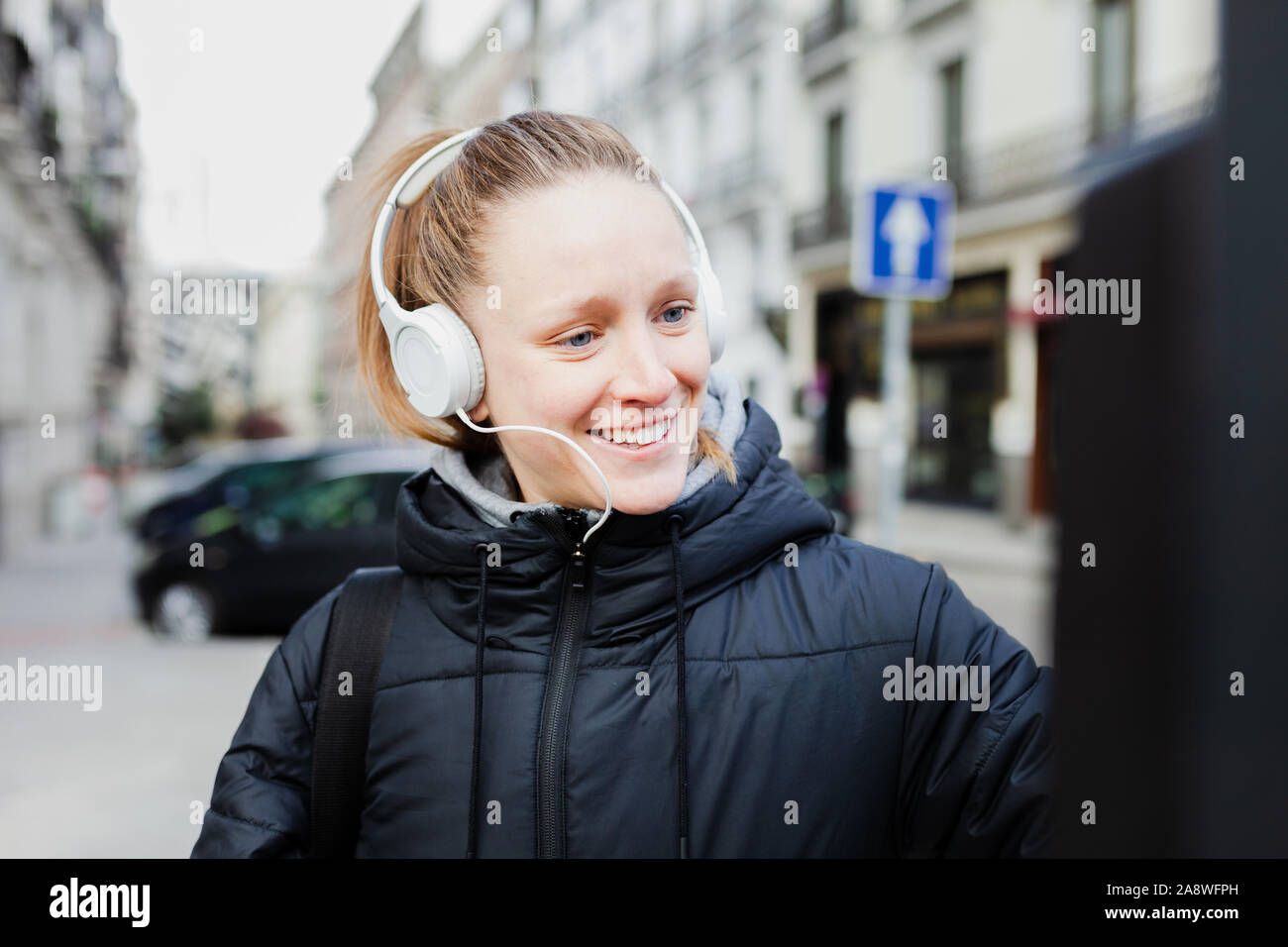 Junge blonde Frau Zahlung auf die parkuhr in der Stadt mit überraschten Gesicht trägt eine Jacke ein Kopfhörer Stockfoto