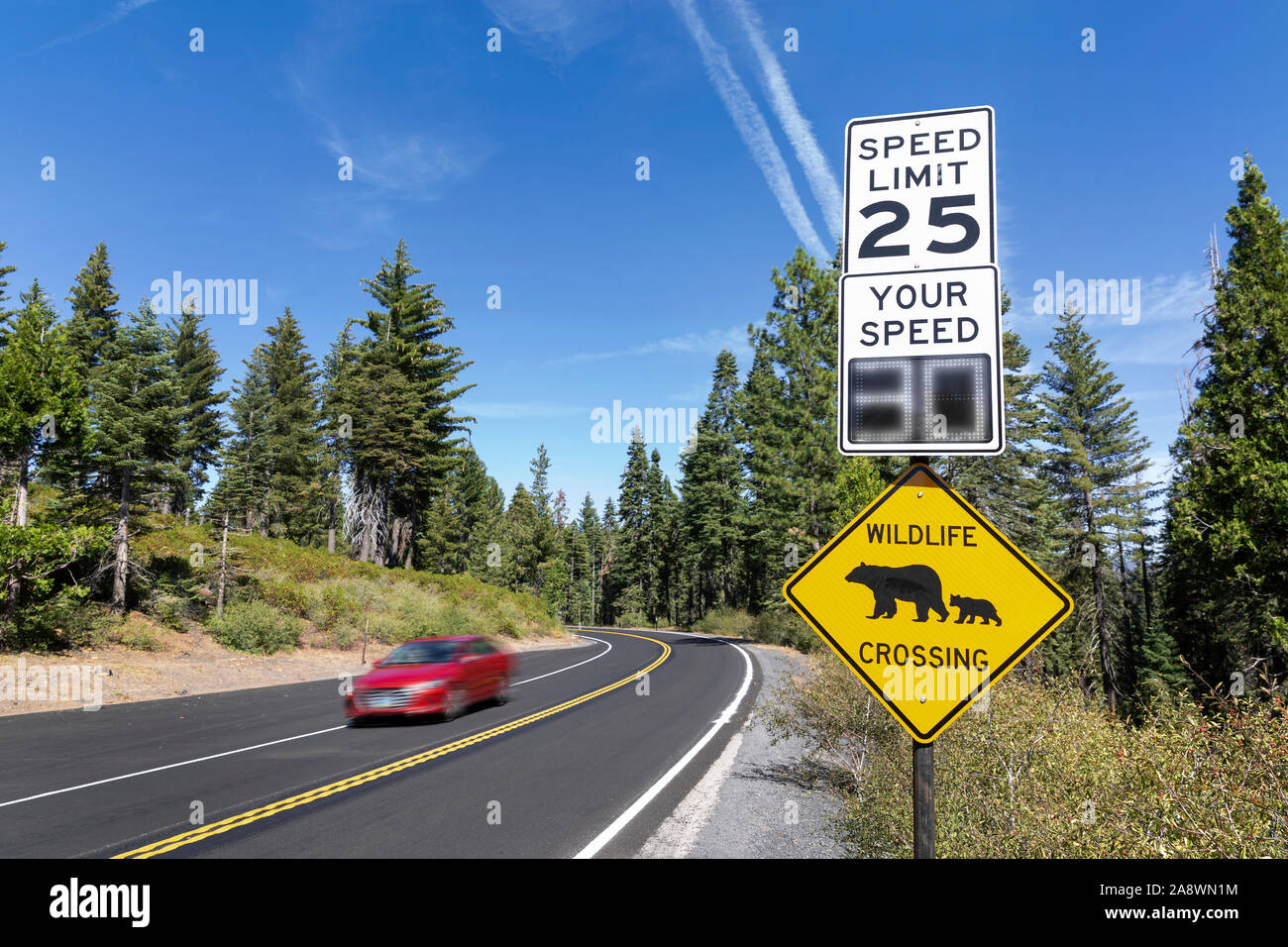 Eine "wildlife Kreuzung' und 25 MPH Höchstgeschwindigkeit Zeichen durch eine Straße mit einem vorbeifahrenden Auto im Yosemite National Park, Kalifornien. Stockfoto