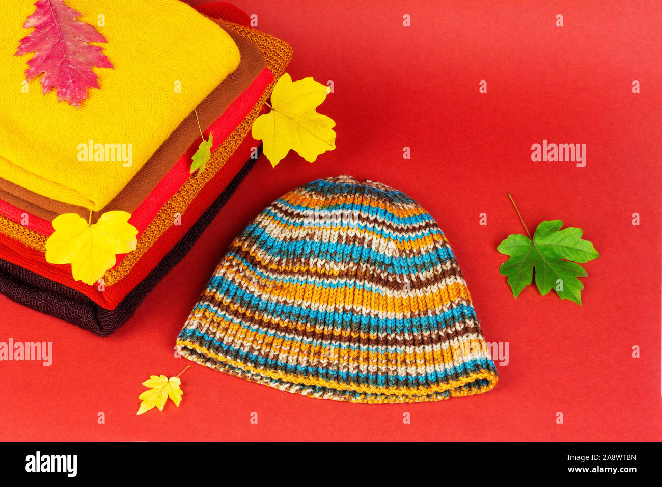 Haufen Frauen Kleidung, warme Herbst Kleidung und Strickmütze mit bunten Herbst Ahorn Blätter auf einem roten Hintergrund, eine Nahaufnahme von oben Stockfoto