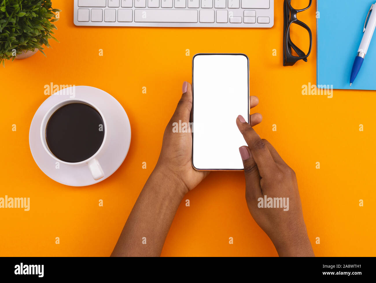 Schwarzes Weibchen mit Smartphone und Kaffee trinken am Arbeitsplatz Stockfoto