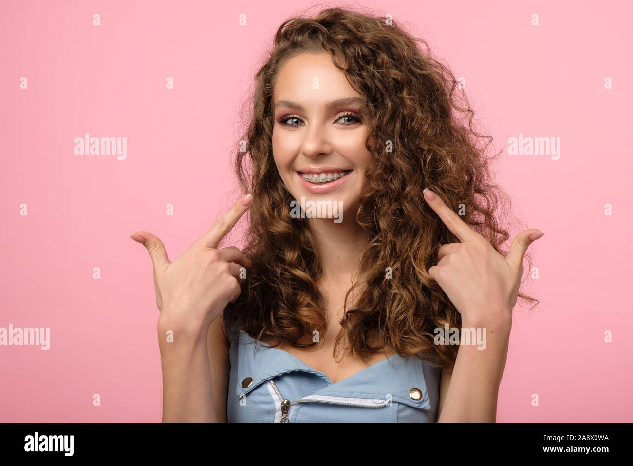 Hübsches Mädchen zeigen ihre zahnspangen mit beiden Händen auf rosa Hintergrund isoliert Stockfoto