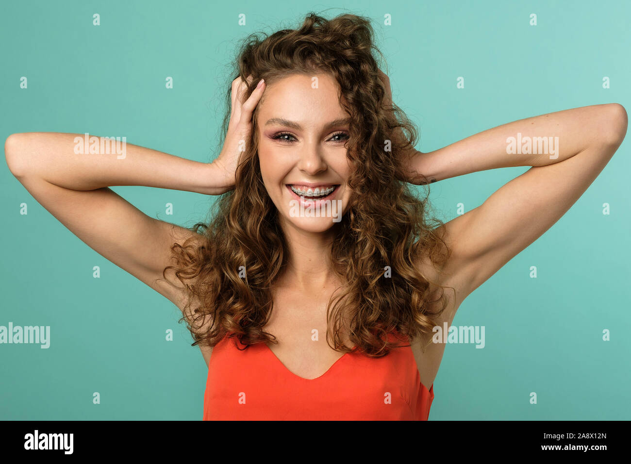 Closeup Portrait von hübschen Mädchen ihren Kopf mit beiden Händen und laut lachen mit Zahnspangen auf Ihren Zähnen auf blauem Hintergrund isoliert Stockfoto