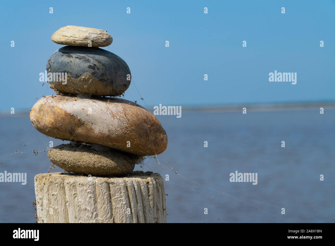 Ein Stapel von bunten Steine auf einem hölzernen Spalte vor der See und den blauen Himmel - Mediation Konzept Stockfoto