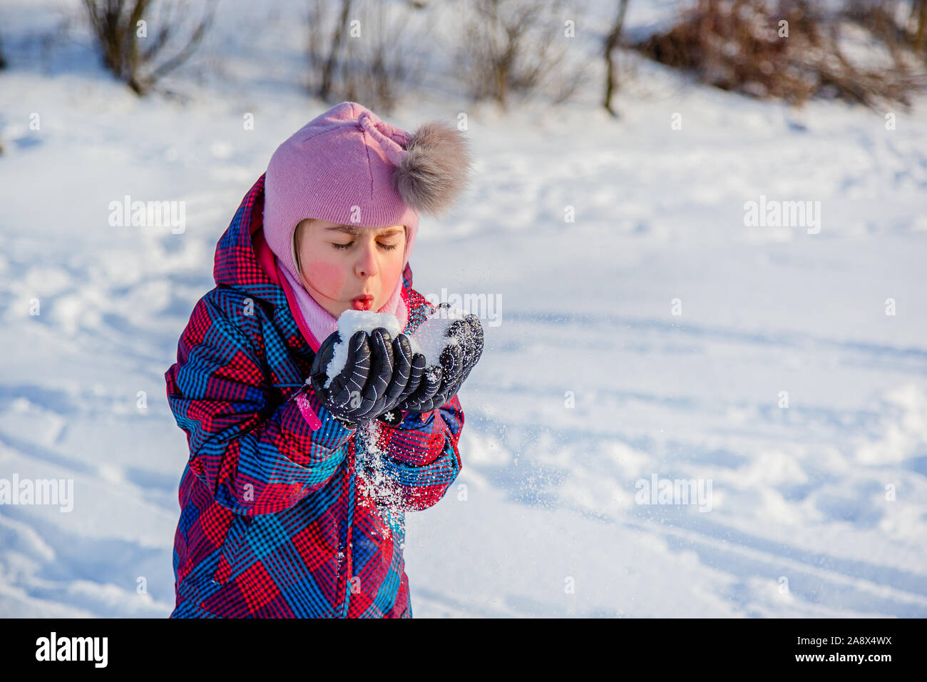 Fröhliches Mädchen wirft Schnee an einem sonnigen Wintertag. Aktive Spiele mit Schnee. Der Winterurlaub. Glückliche Kindheit. Stockfoto
