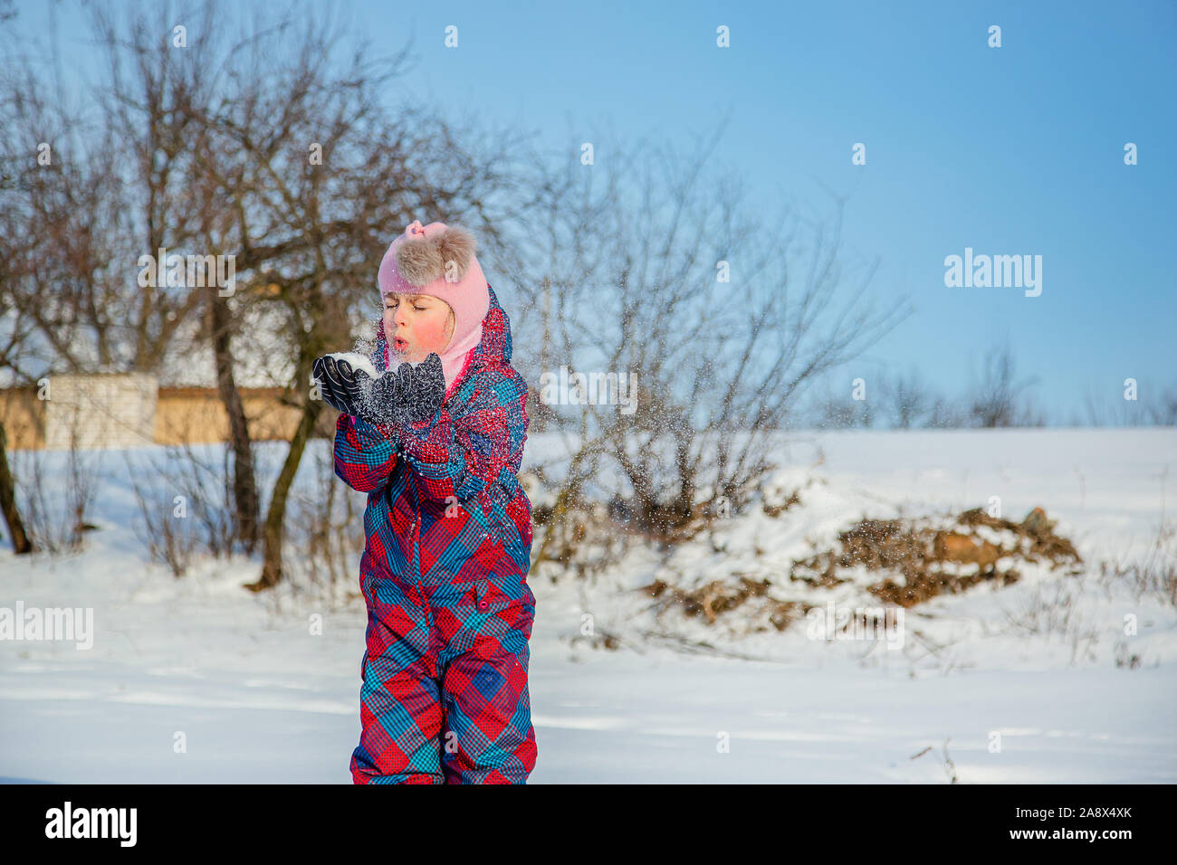 Fröhliches Mädchen wirft Schnee an einem sonnigen Wintertag. Aktive Spiele mit Schnee. Der Winterurlaub. Glückliche Kindheit. Stockfoto