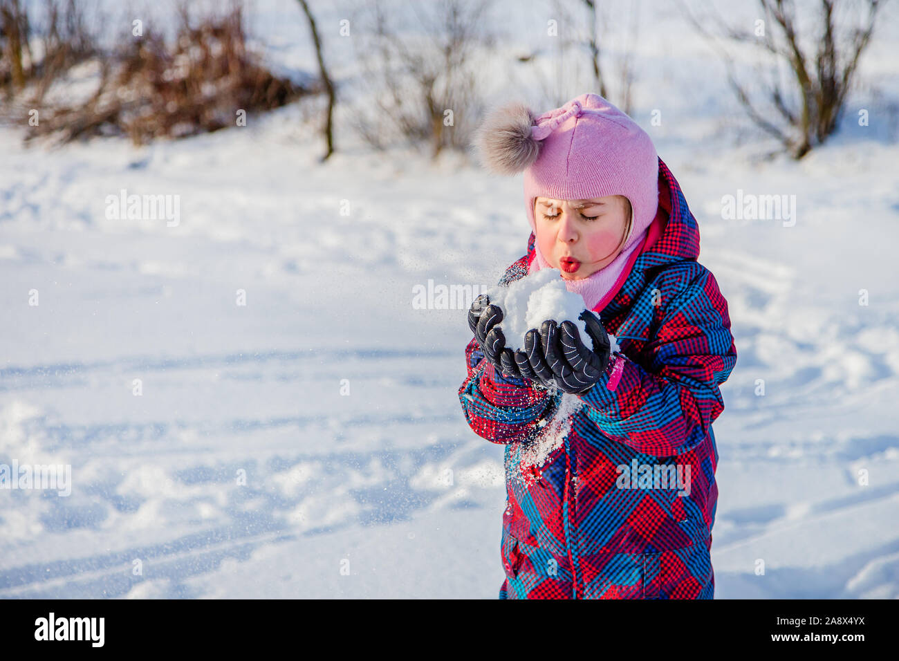 Fröhliches Mädchen wirft Schnee an einem sonnigen Wintertag. Aktive Spiele mit Schnee. Der Winterurlaub. Glückliche Kindheit. Stockfoto