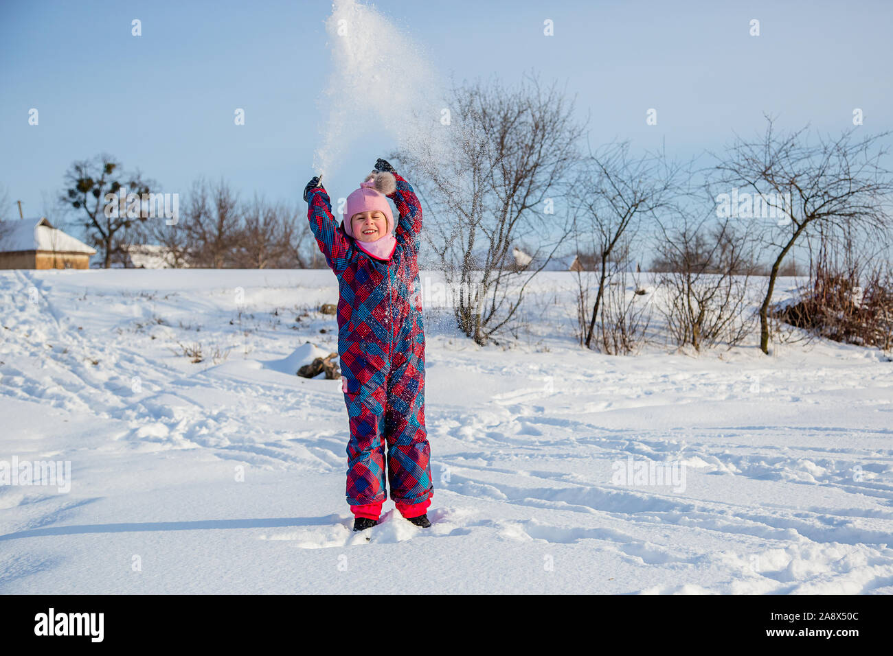 Fröhliches Mädchen wirft Schnee an einem sonnigen Wintertag. Aktive Spiele mit Schnee. Der Winterurlaub. Glückliche Kindheit. Stockfoto